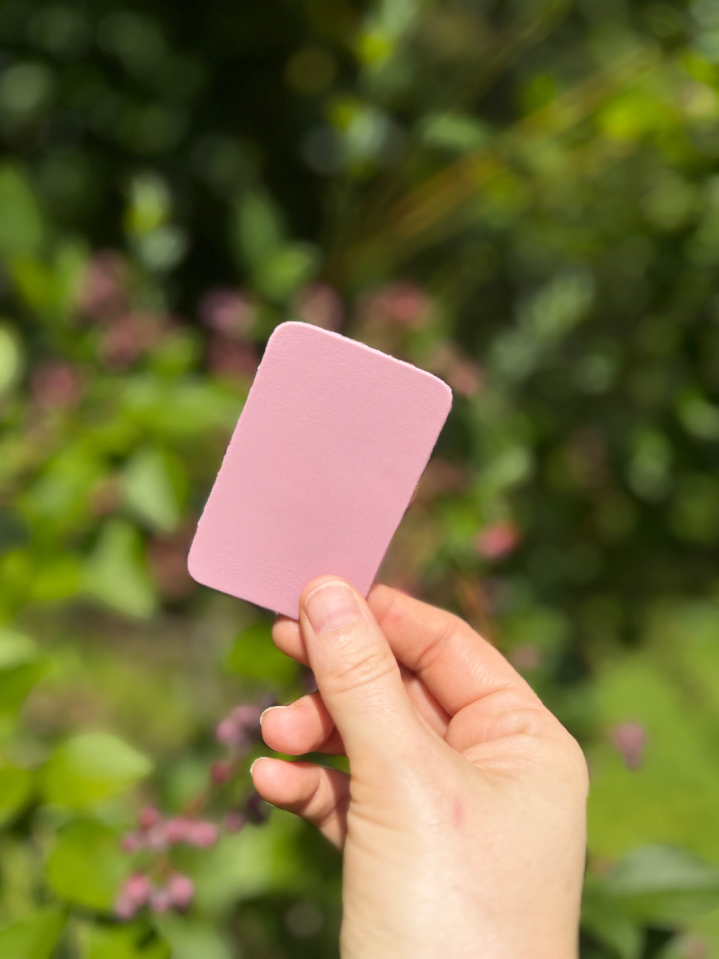 Hand holding a purple-pirnk leather piece against a blurred green outdoor background