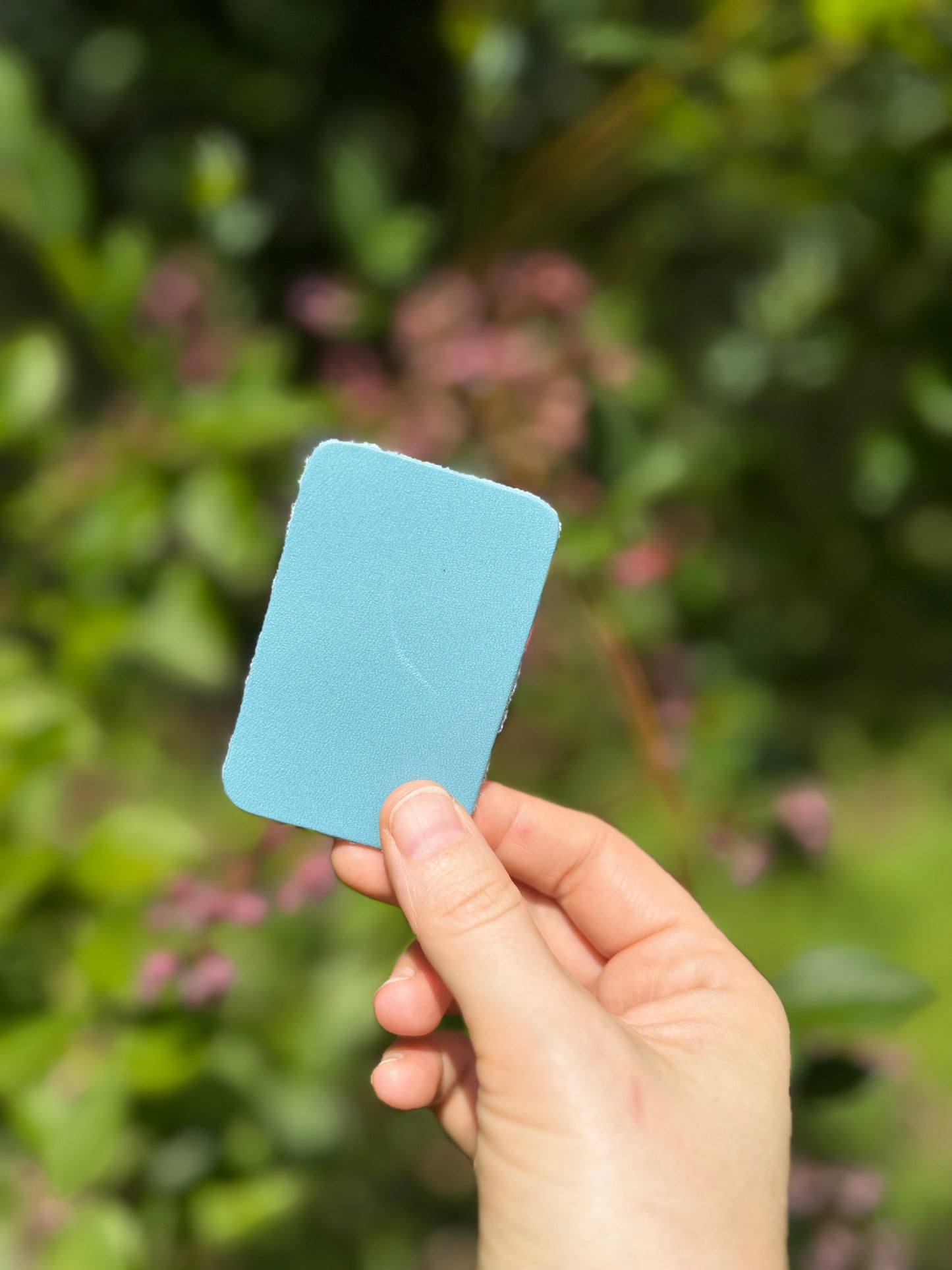 Hand holding a blue leather piece against a blurred green outdoor background