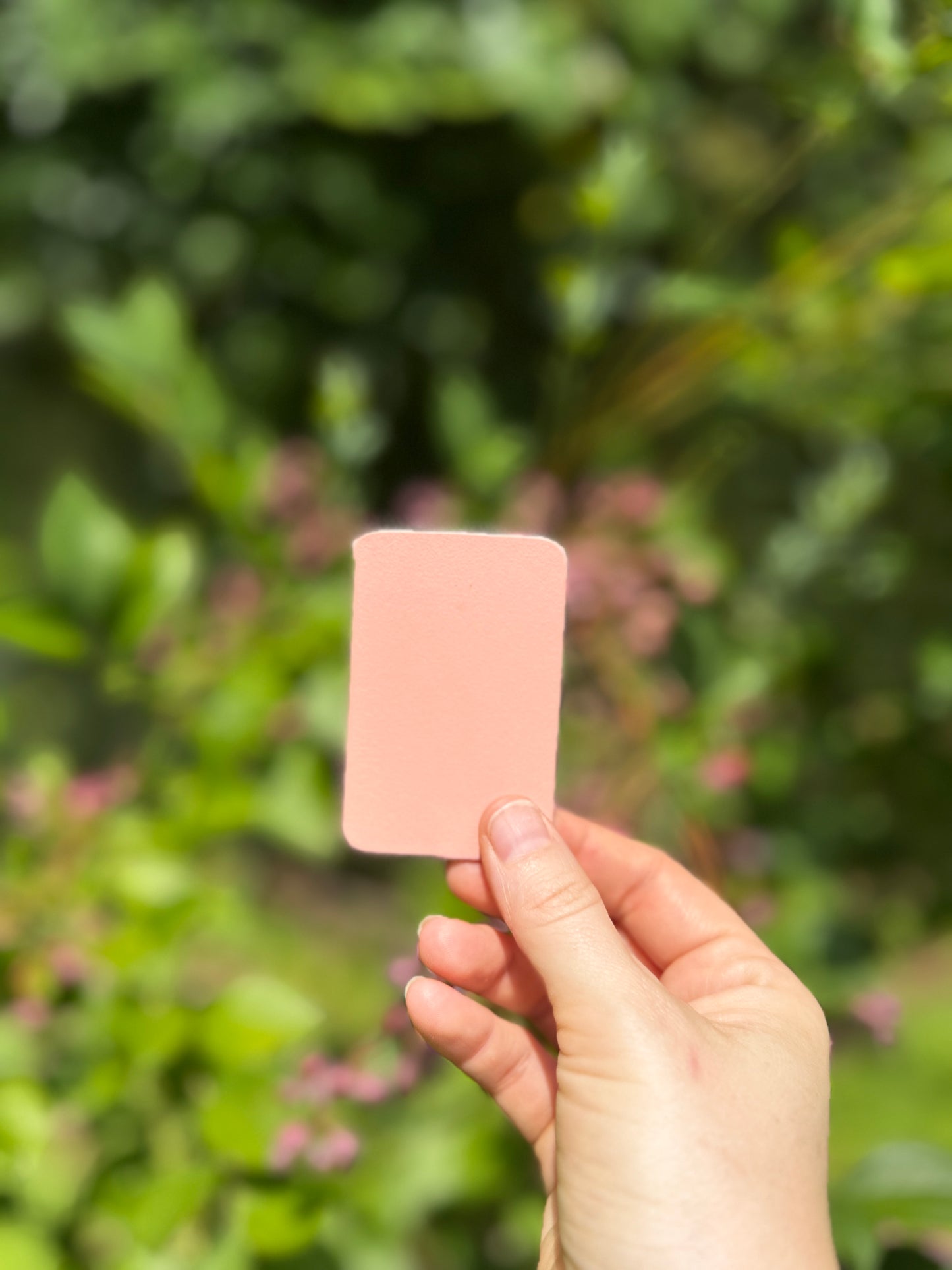 Hand holding a pink leather piece against a blurred green outdoor background