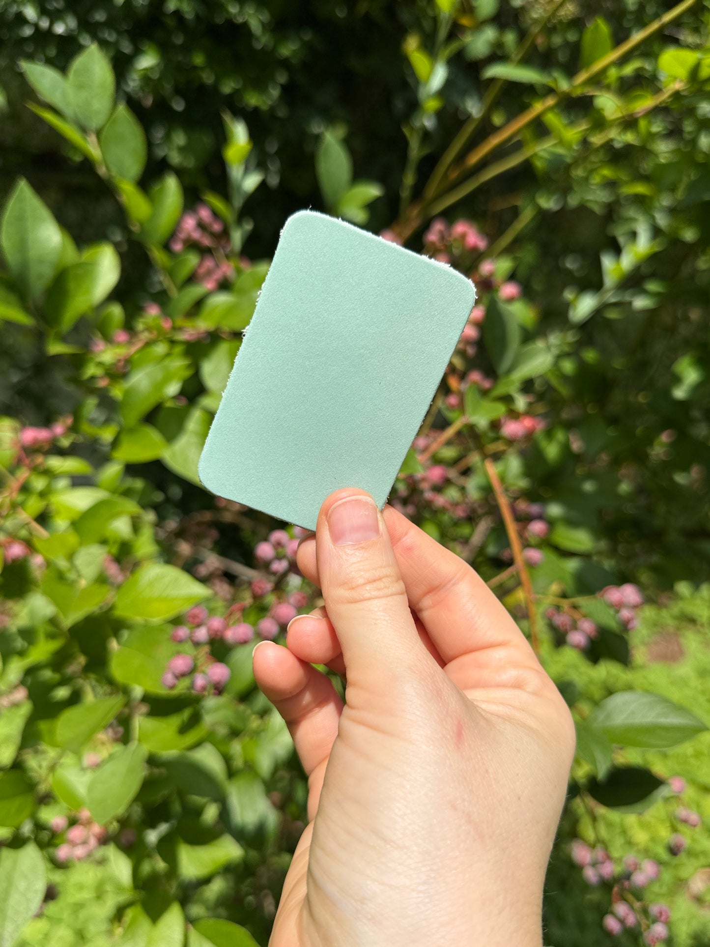 Hand holding a sea foam green leather piece against a blurred green and pink background