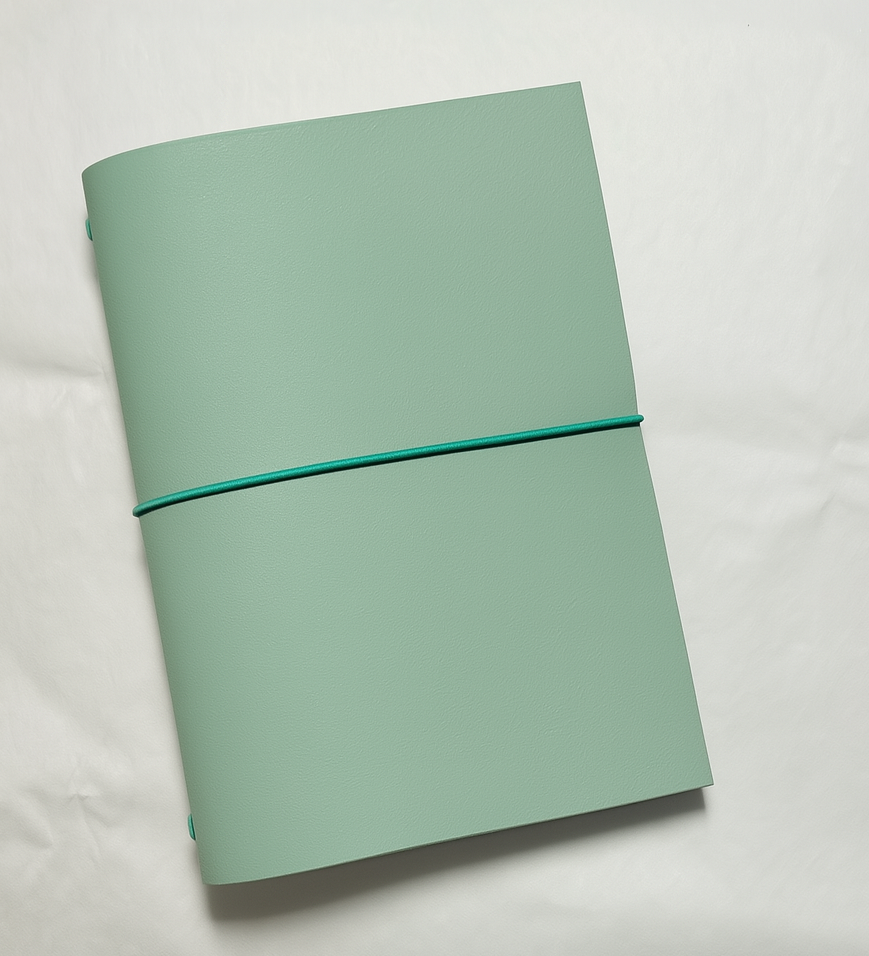 Seafoam green notebook with a teal elastic band on a light gray background