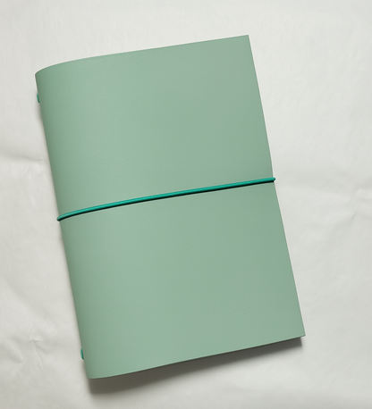 Seafoam green notebook with a teal elastic band on a light gray background