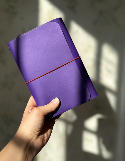 Hand holding a purple notebook with a red strap against a light background
