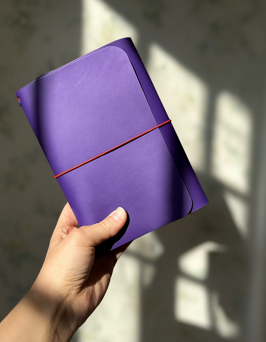 Hand holding a purple notebook with a red strap against a light background
