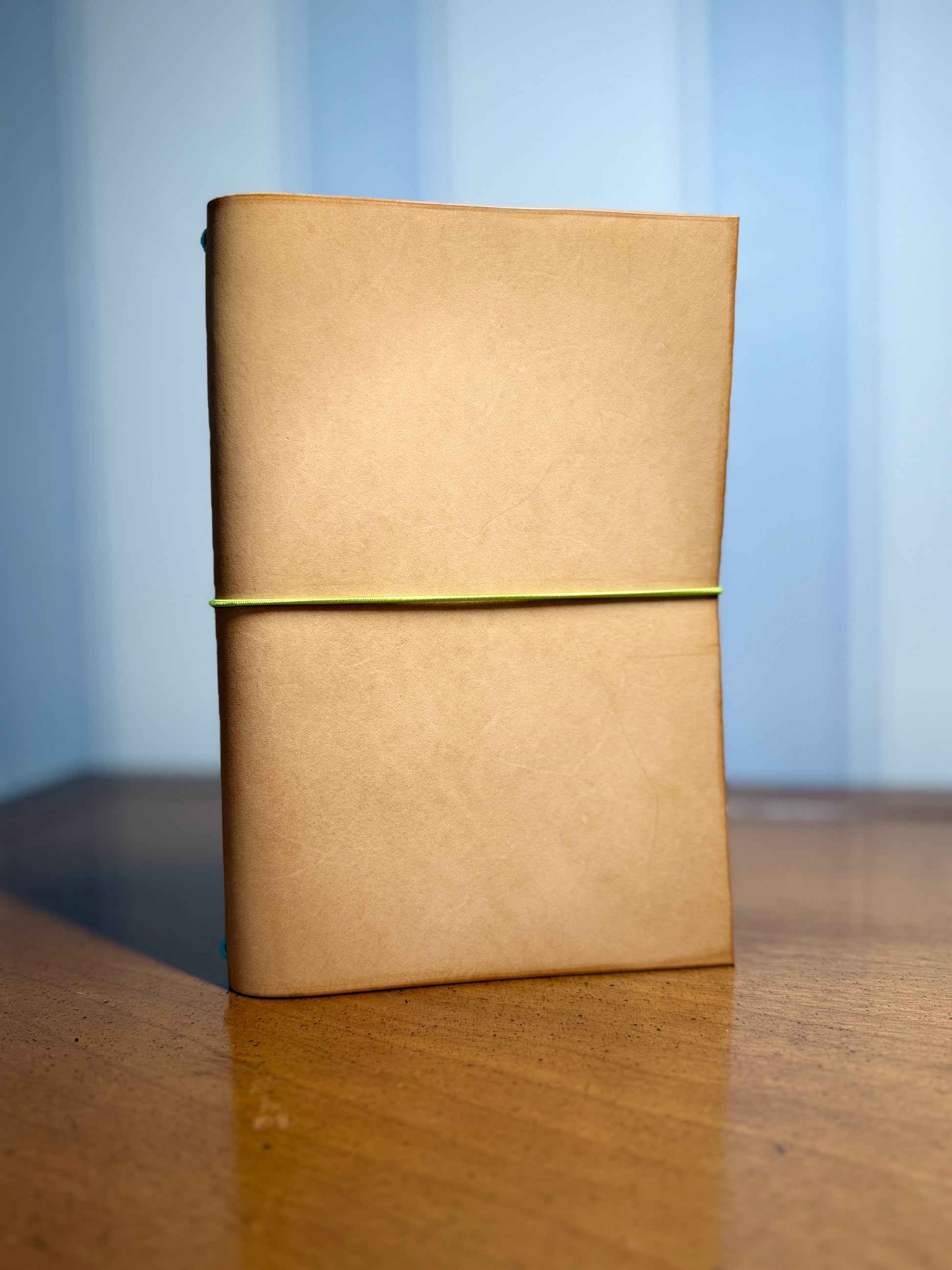 Natural leather notebook with a bright green elastic band on a wooden surface with a blue gradient background