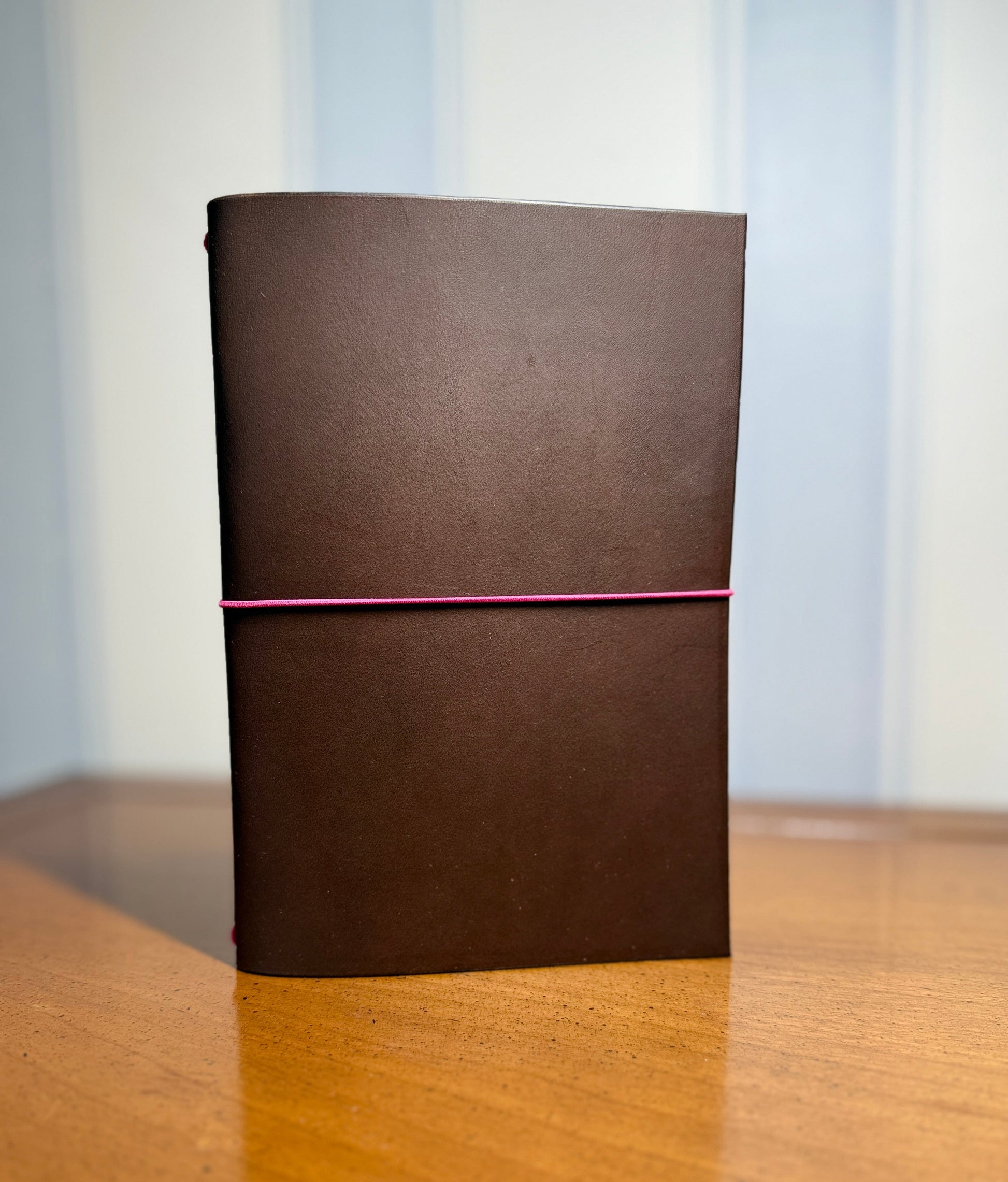 Brown leather-bound book on a wooden surface with a light blue wallpaper background