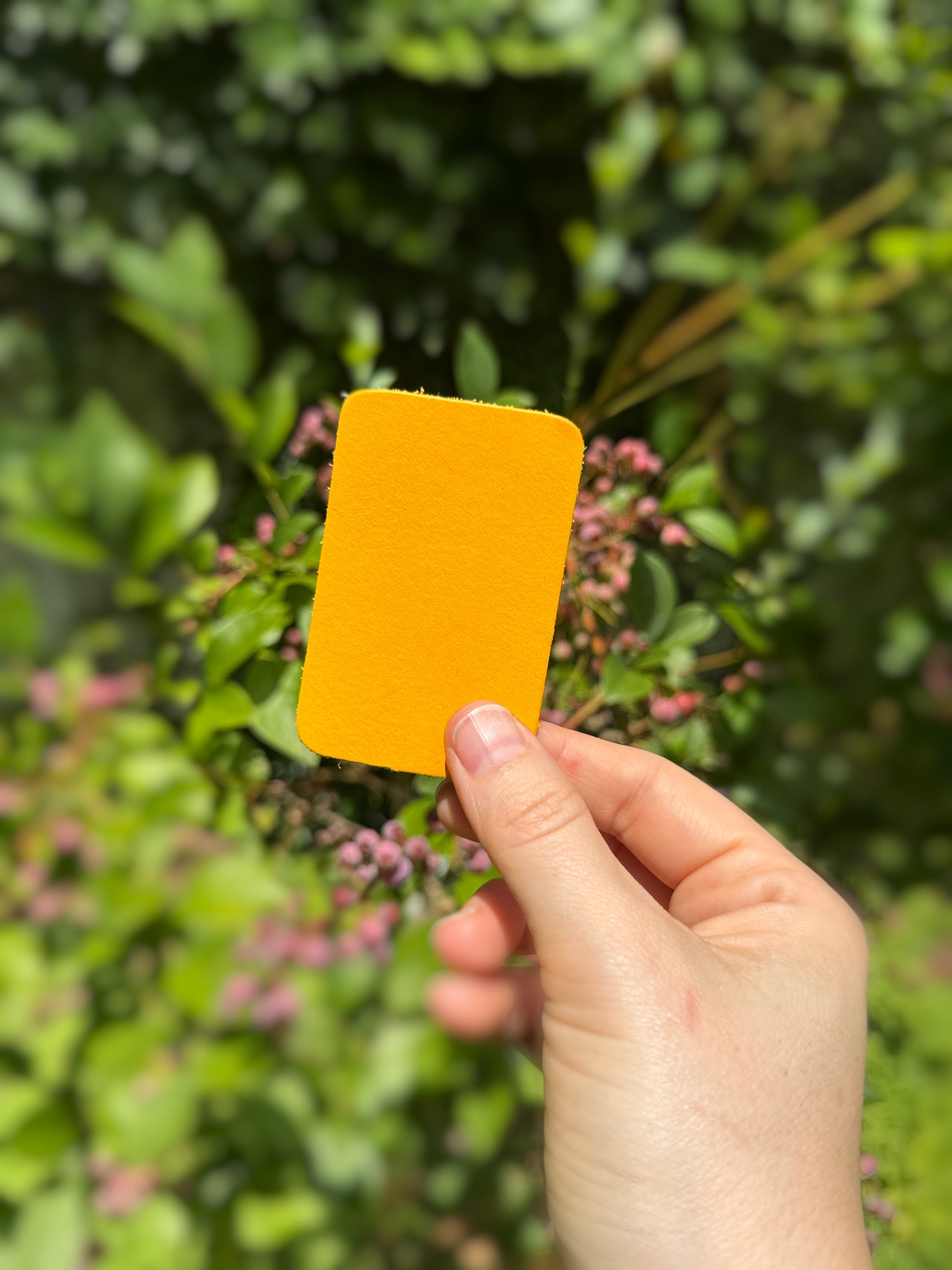 Hand holding a lemon yellow leather piece against a blurred green and pink background