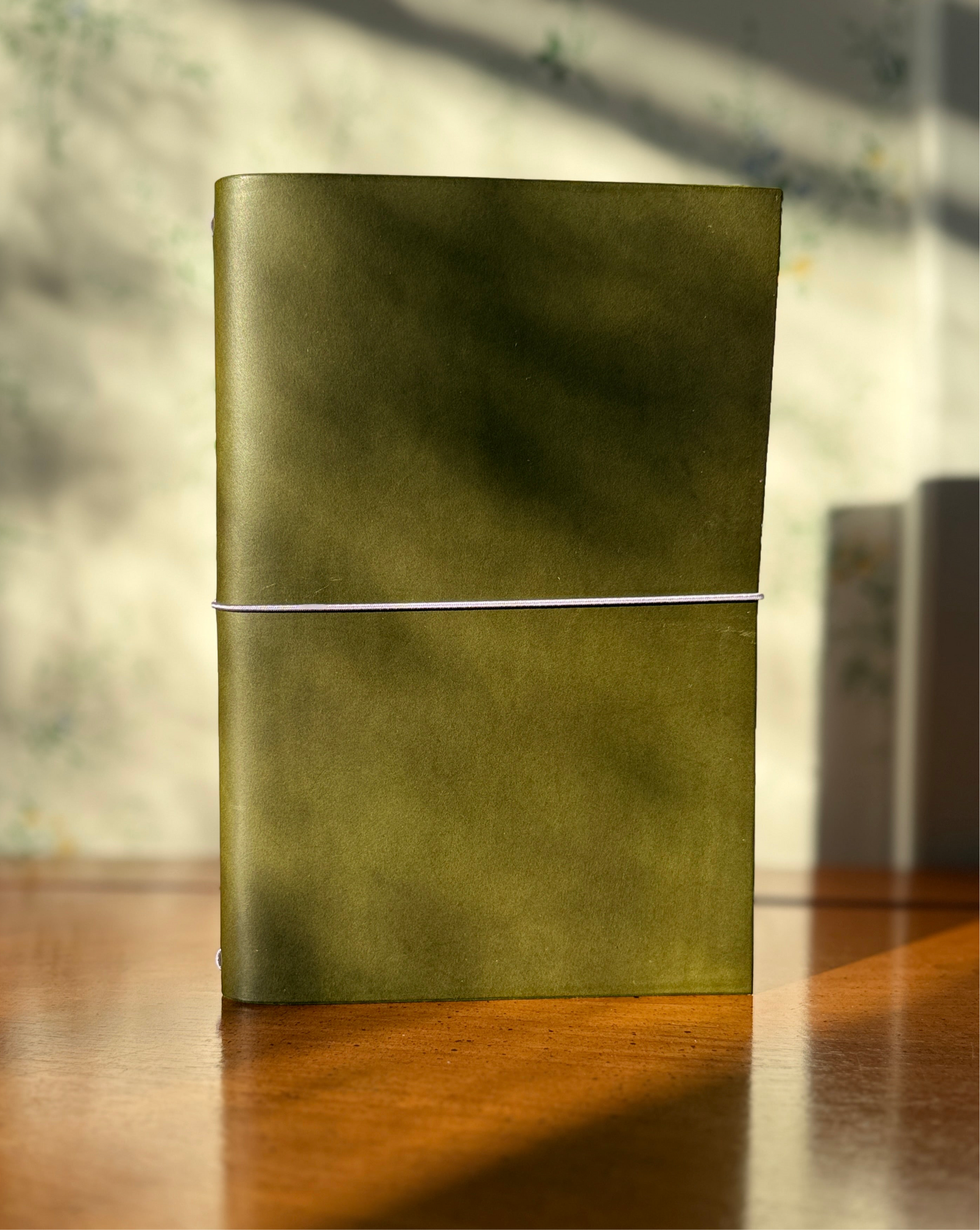 Green leather notebook on a wooden surface with a blurred background