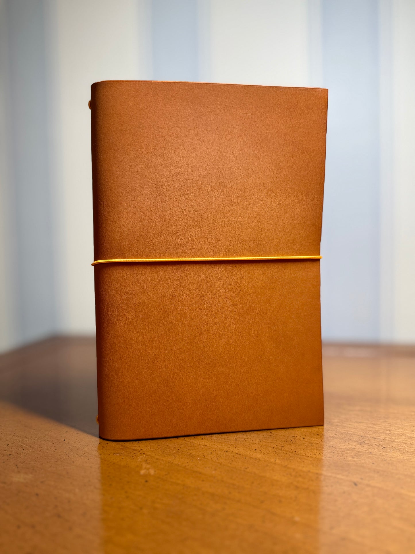 Light-brown leather notebook with a gold elastic band on a wooden surface