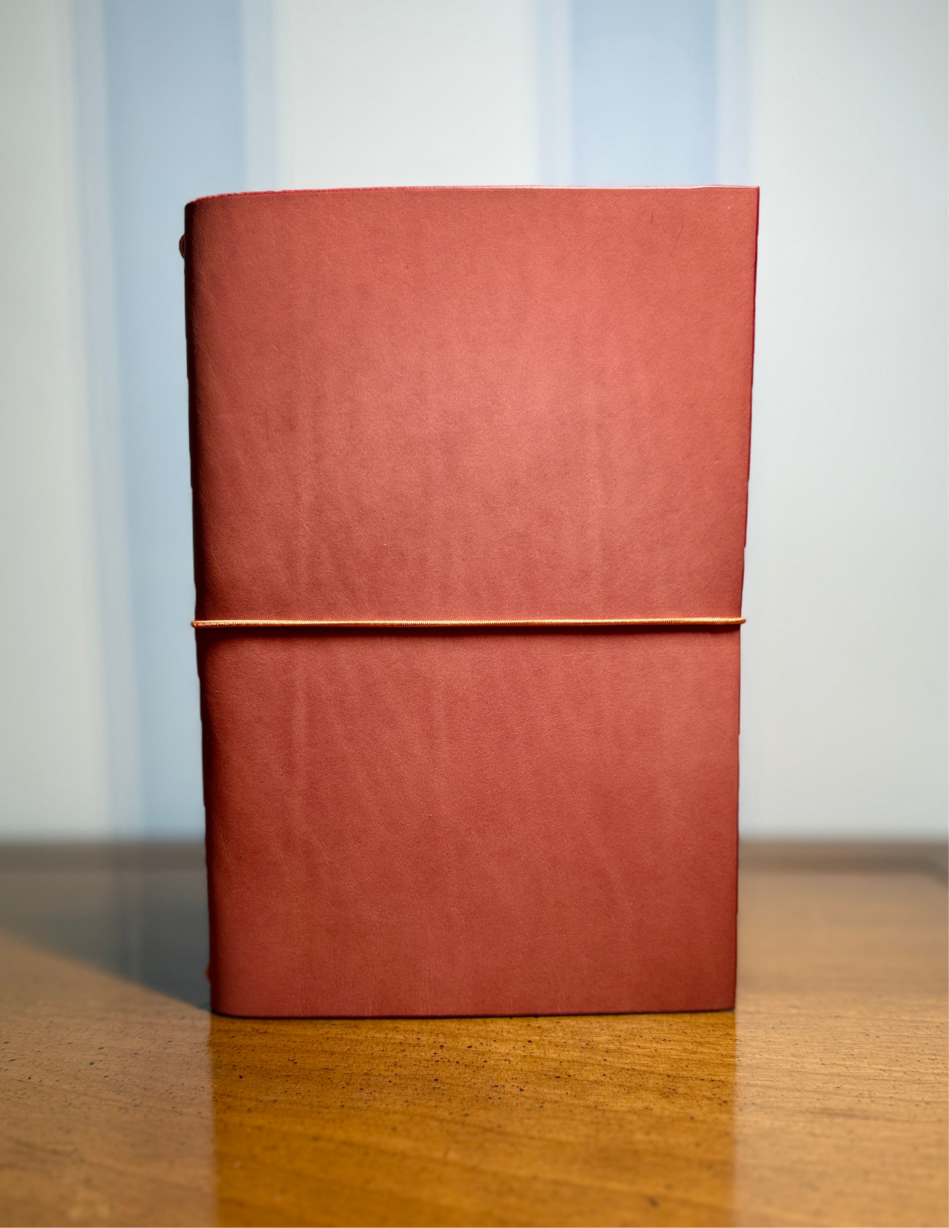 Pink  notebook with a pale peach elastic band on a wooden surface and light blue wallpaper background