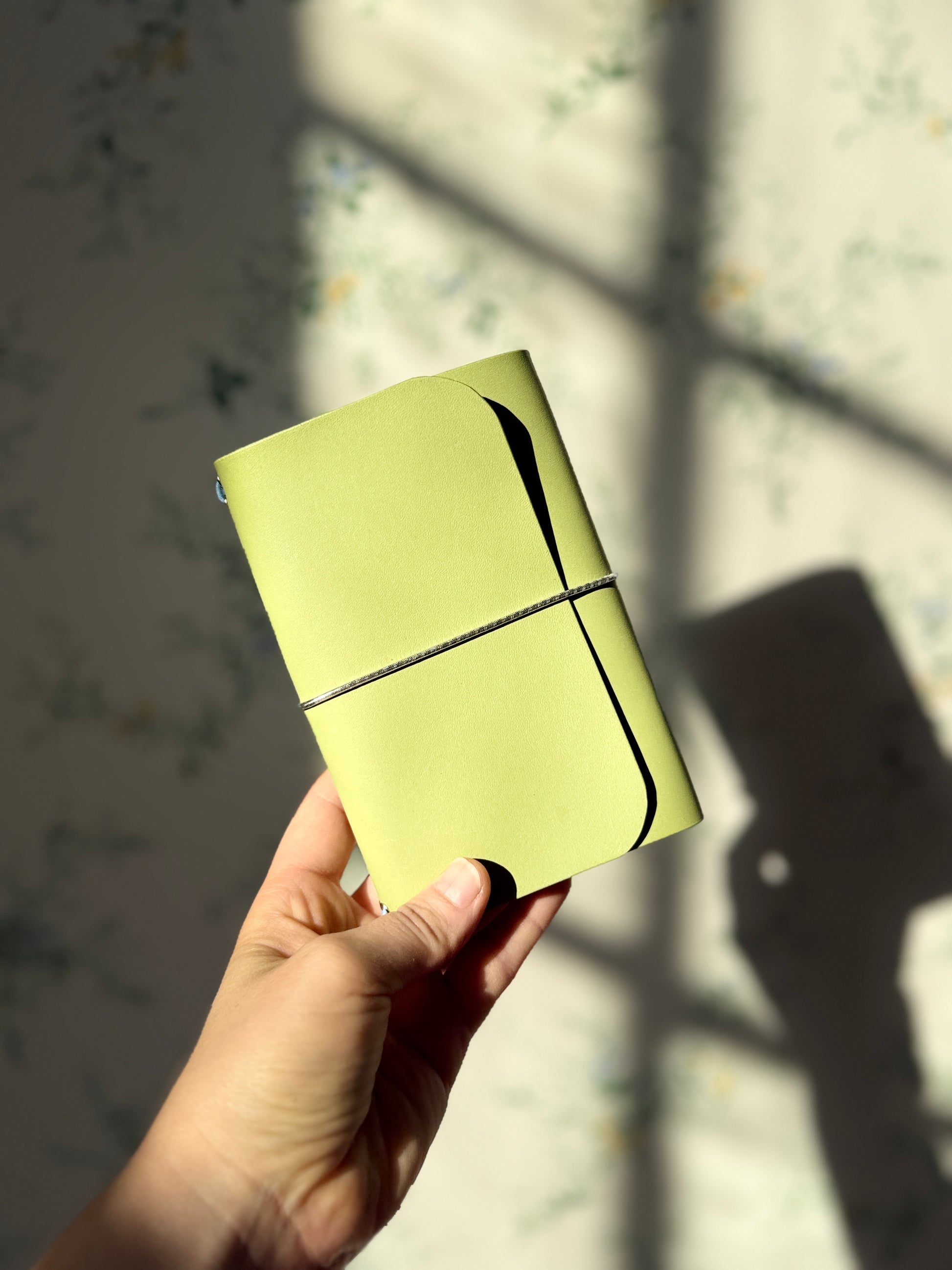 Hand holding a light green journal against a neutral background