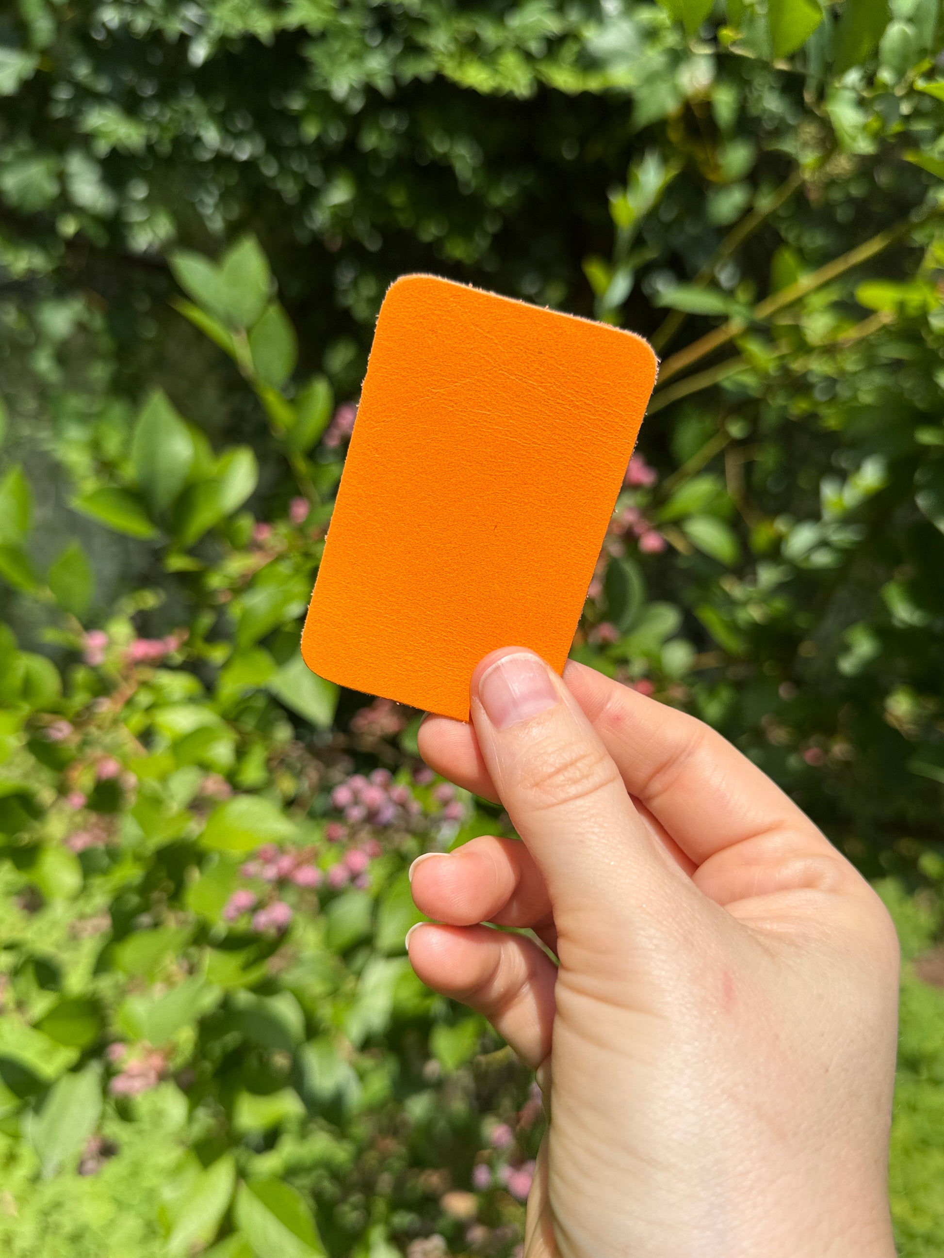 Hand holding an orange leather piece against a green leafy background