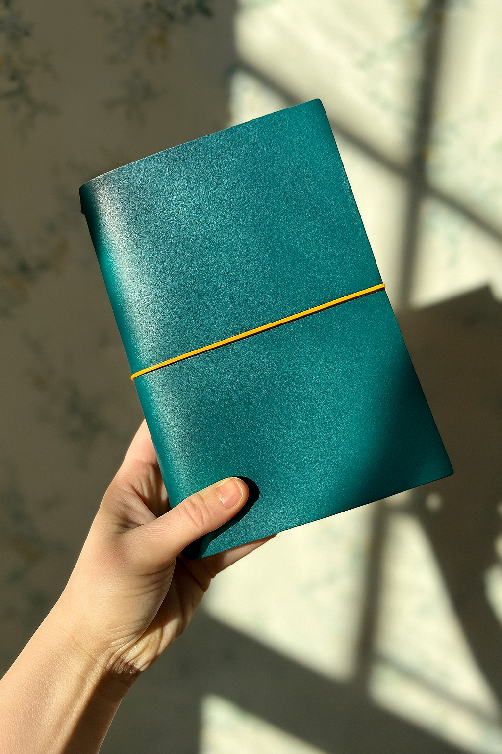 Teal notebook with a yellow strap held by a hand on a light background